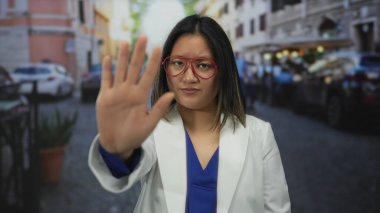 Şehirde gözlüklü, beyaz önlüklü ve mavi gömlekli bir kadın elini açık tutmayı kesiyor..