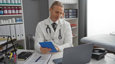 Klinikteki doktor, tıbbi ekipman ve dosyalarla çevrili steteskopla, beyaz erkek profesyonelin bulunduğu kapalı bir hastane ortamında, klinikteki tableti analiz ediyor..