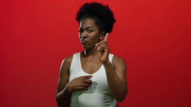 Kadın kendini gösterir ve işaret eder. Hayır parmağıyla, izole edilmiş kırmızı bir arka planda durur. Renkli ve anlamlı bir ortamda kendine güvenini ve özgüvenini somutlaştırır..