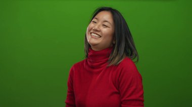 Neşeli bir şekilde gülümseyen genç bir kadın canlı yeşil bir duvara karşı neşeli bir şekilde, pozitif enerjisini ve tarzını sergiliyor..