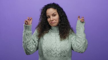 Yeşil kazaklı İspanyol bir kadın parmaklarıyla tırnak işareti yapıyor, mor bir arka plana karşı duruyor, belirsizlik ve iğnelemeyi ifade ediyor..