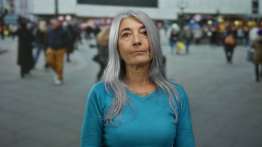 Şehir dışında kalabalık bir sokakta, hareketli insanlarla çevrili, gri saçlı son sınıf öğrencisi kadın, şehir hayatını ve yaş farkını aktarıyor..