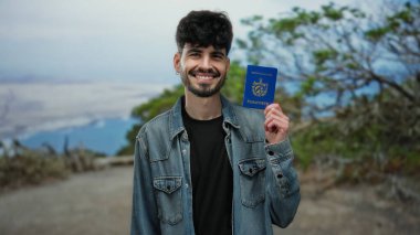 Sahilde elinde Küba pasaportu olan arka planda su olan kot ceketli bir adam..