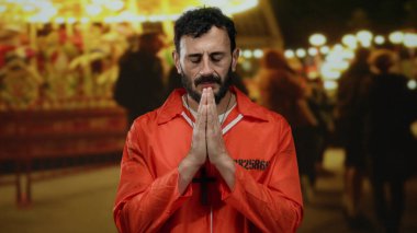 Turuncu tulumlu İspanyol bir mahkum, sakallı bir panayır atlıkarıncasında dua ediyor, neşeli bir şenlik ortamı ile yan yana hapsediliyor..