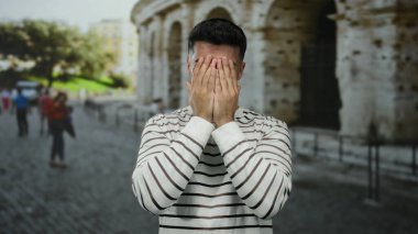 Genç adam, Roma Stadyumu 'na gülümseyip şakacı bir şekilde yüzünü örtüyor. Roma' nın ikonik açık hava ortamında neşeli bir an sergiliyor..