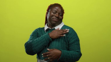 İzole edilmiş sarı bir arka plana gülümseyen, yeşil bir kazak giyen, hareketleriyle kendine güvenini ve güvenini ifade eden bir kadın..