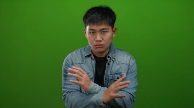 Kot ceketli genç adam, yeşil arka plana karşı olumsuz duygular besliyordu. Elleri çapraz olsun ya da olmasın, bir anlaşmazlık vardı..