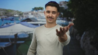 Şehir merkezindeki bulanık geçmişi olan Latin kökenli genç adam açık mavi gökyüzü altında davetkar bir jest sergiliyor.