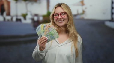 Elinde Romen lei banknotları tutan genç bir kadın şehir sokaklarında neşeli bir ifadeyle para gösteriyor..