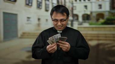 Papaz kıyafeti giymiş gözlüklü bir adam şehir merkezindeki açık hava ortamında bize dolar banknotları tutuyor ve şehirde heyecanlı bir yüz ifadesi var..