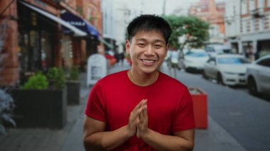 Şehir caddesinde kırmızı tişört giyen genç adam arka planda arabalar ve binalarla açık havada duygularını ifade ediyor..