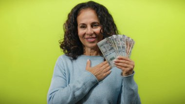 Perulu orta yaşlı bir kadın tek eli göğsünde Perulu tabanlar tutuyor. Parlak sarı bir arka plana gülümsüyor..