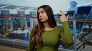 Yolcu gemisindeki yeşil tişörtlü kadın, bir liman zeminine karşı ciddi bir ifadeyle parmak tabancası hareketi yapıyor..