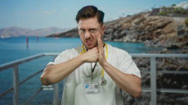 Steteskoplu genç, beyaz sakallı doktor sahilde güneşli bir günde deniz kenarında medikal profesyonelliği deniz kenarına karıştırarak savaş jesti yapıyor..