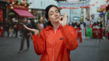Yoğun caddede turuncu tulumlu bir kadın, açık hava şehir sahnesinin ortasında kendine güveni olan oyuncu bir tabela ile el kol hareketi yapıyor..