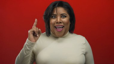 Kırmızı arka planda parmakları yanaklarında fikri ifade eden, düşünceli ve mutlu duygular gösteren, izole bir ortamda, artı boyut ve İspanyol kimliğini vurgulayan bir kadın..