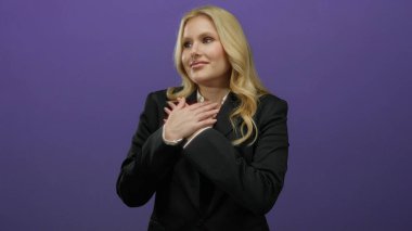 Minnettarlığını ifade eden bir kadın, elleri göğsünde koyu mor bir arkaplan karşısında, resmi siyah bir spor ceketle, samimi bir duyguyu somutlaştırıyor..