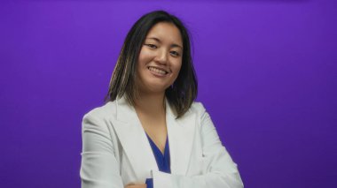 Genç Çinli kadın, kolları bağlı bir şekilde parlak mor bir arka plana karşı duruyor ve modern bir ortamda profesyonellik ve karizma yayıyor..