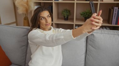 Kadın rahat oturma odasında selfie çekiyor modern dekorasyon ve şık döşemelerle rahat ve rahat bir atmosfer sergiliyor..