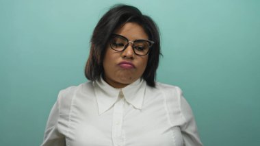 Gözlüklü ve beyaz gömlekli kadın, modern tarz ve duygulara odaklanmış saf mavi bir arkaplan karşısında düşünceli bir ifade sergiliyor..