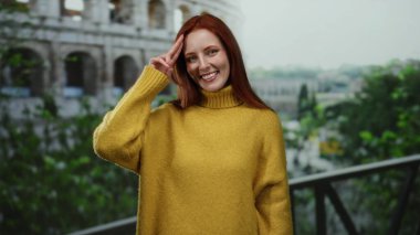 Roma Kolezyumu 'nun önünde kızıl saçlı, sarı kazaklı bir kadın güneşli bir günde yeşil bir ortamda canlı bir açık hava yaratıyor..