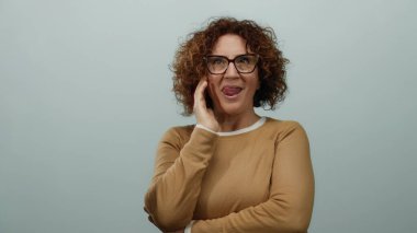 Orta yaşlı bir kadın, izole edilmiş beyaz duvara karşı komik bir yüz ifadesi sergiliyor. Kişiliği ve duyguları neşeli bir şekilde vurguluyor..