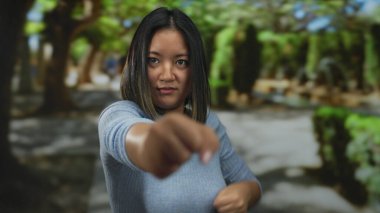 Parkta dövüş sanatları uygulayan genç bir kadın, gücünü sergiliyor ve sakin açık hava ortamının ortasında, dinamik hareketini ve yoğunluğunu doğal ortamında yakalıyor..