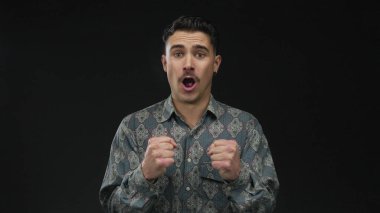 İzole edilmiş siyah arkaplan duvarına karşı duygularını ifade eden genç bir adam değişik ruh hallerinde desenli bir gömlek giyiyor dinamik ifade ve stil aktarıyor.