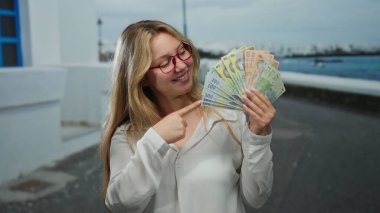 Romanyalı kadın deniz kenarındaki gezinti alanında neşeli bir ifadeyle finans başarısının özünü yakalıyor..