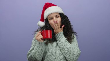 Noel Baba şapkası ve kazağı giyen kadın, kırmızı bardağı mor arka planda tutarken öpüşüyor. Neşeli bir ifade ve rahat bir atmosferle bayram ruhunu kucaklıyor..