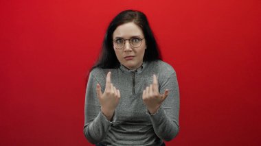 Esmer kadın, koyu kırmızı arka planda, gözlüklü ve gri kazaklı bir kadına şaşkınlık ve şaşkınlık içinde bakıyor..