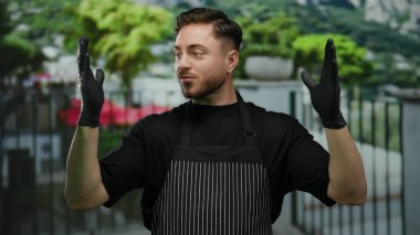 Sakallı, eldiven takan ve önlük takan genç bir adam şehir caddesinin büyüklüğünü belirtmek için yeşil arka planı bulanık..