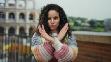 Renkli kazaklı, kıvırcık saçlı genç İspanyol kadın Roma, İtalya 'daki sembolik Roma kolezyumunun önünde kollarını kavuşturuyor..