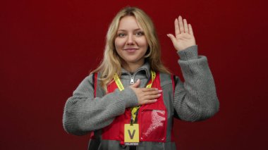 Kırmızı arka planda kırmızı yelek giyen, kendine güvenen ve gururlu bir kadın..