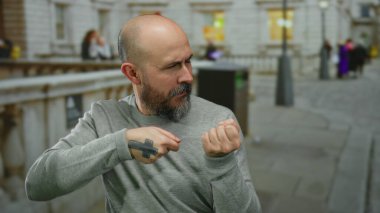 Kel sakallı bir adam, şehir sokaklarında görünmez bir halatı çekiyor, açık havada oyuncu davranışlar sergiliyor..