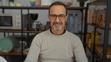 Odanın içinde rahat bir şekilde gülümseyen olgun İspanyol bir adam. Arkaplanda raflar ve kavanozlar var.