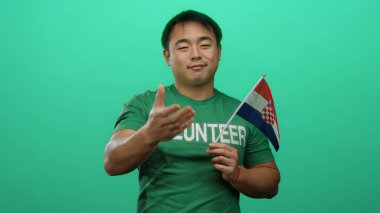 Genç adam, gönüllü gömleği giyerken yeşil arka planda bir Hırvat bayrağı tutuyor..