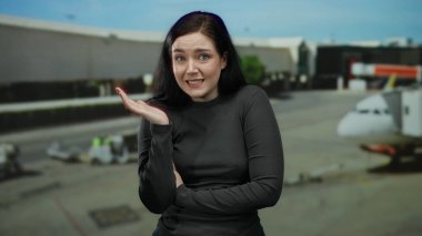 Esmer bir kadın havaalanında sürpriz ve endişeyi dile getiriyor, arka planda seyahat etmeyi simgeleyen görünen bir uçakla yoğun bir seyahat ayarını vurguluyor..