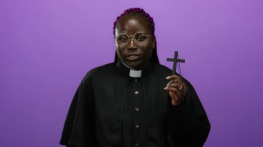 Canlı mor arka planda haç tutan kadın rahip, dinsel kıyafetlerle güvenle gülümsüyor.