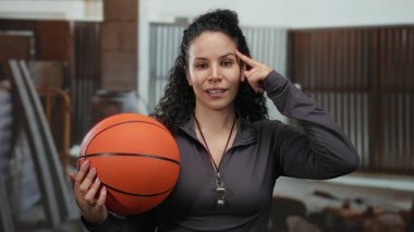 Kapalı alanda basketbol oynayan, ıslık çalan, siyah kıyafetler giyen, gülümseyen, İspanyol, düşünen, kıvırcık saçlı, iş yerinde çalışan bir kadın..