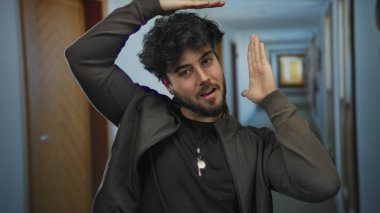 Sakallı enerjik genç bir adam otel koridorunda el hareketleriyle yaratıcılığı ve heyecanı gösteriyor..