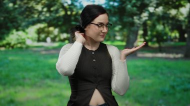 Parkta bir kadın, elinde yeşil doğal arka plana karşı bir şey sunarak sükuneti ve doğayı bir gülümseme ve günlük kıyafetle öneriyor..