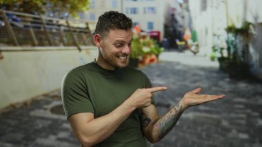 Yeşil gömlekli genç adam şehir caddesinde duruyor. Dövmesi görünür, canlı şehir zeminiyle çevrili, odaklanmış bir ifadeyle modern şehir yaşamını gözler önüne seriyor..