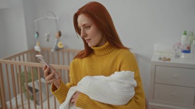 Sıcak yatak odasında beşiğiyle telefon kullanırken kucağında bir kadın, sıcak ev ortamında modern annelik temalarını sergiliyor..