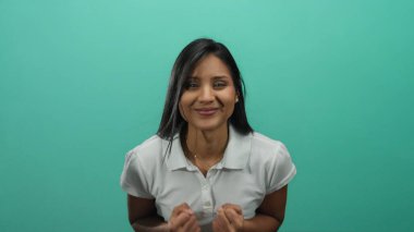 Yeşil bir arka plana güvenerek gülümseyen, beyaz polo giyen, pozitif ve coşkulu ifade eden, gençlik enerjisi ve mutluluğunu gösteren bir kadın..