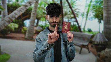 Zengin bir açık hava parkında İspanyol pasaportu taşıyan bir adam, çevresindeki yeşillikle seyahat ve kimliğe vurgu yapıyor..