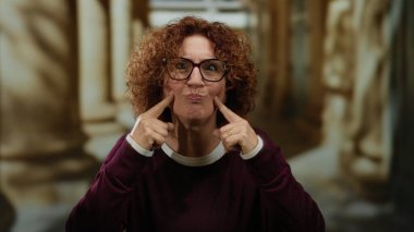 Kıvırcık saçlı, gülümseyen ve üniversite ortamında el kol hareketi yapan bir kadın akademik ortamda neşe saçıyor..