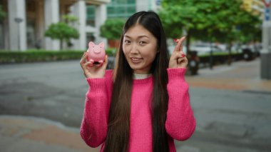 Pembe kazaklı kadın domuz kumbarası tutuyor ve şehir caddesinde şans ve tasarrufu simgeliyor..