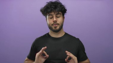 Genç sakallı, gözleri kapalı, canlı mor bir arka plana karşı meditasyon pozu veren sakin ve konsantre bir adam.