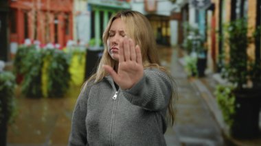 Sonbaharda şehir caddesinde elini kolunu sallayarak gezen kadın bulanık şehir çevresiyle çevrili gri bir kazak giyiyor. Açık havada ifade ve vücut diline odaklanılmasını öneriyor..